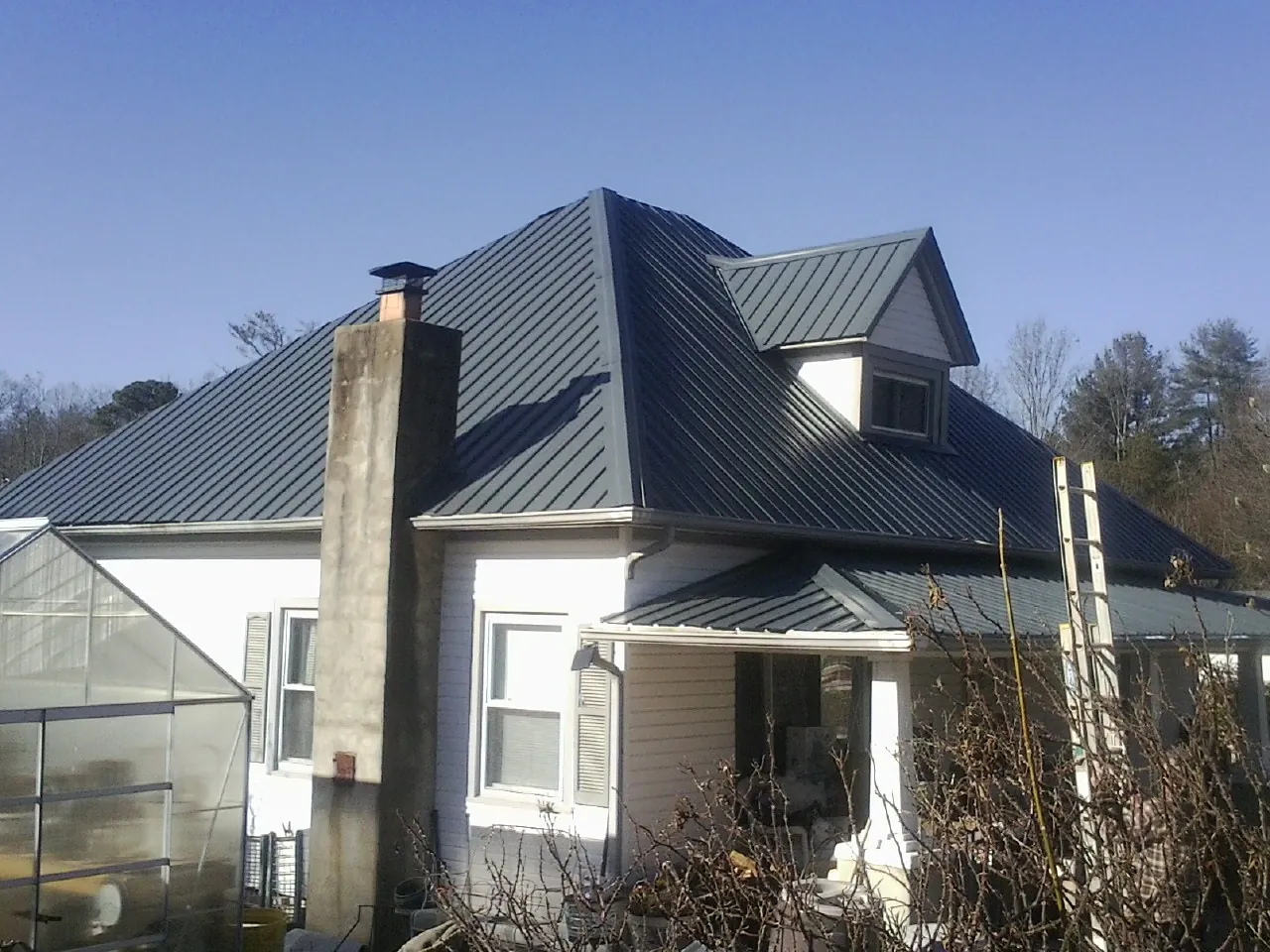 Dark blue standing seam metal roof on a white farmhouse with dormer — Slate & Tile Roof Repair by Roofing Brothers in Glen Cove