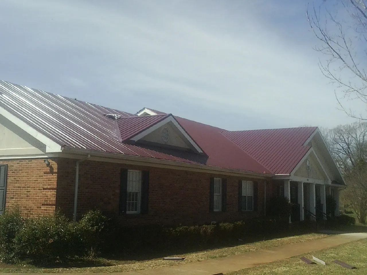 Red metal roof with gabled entries on a long brick building, from a Hail Damage Roof Repair job in Glen Cove