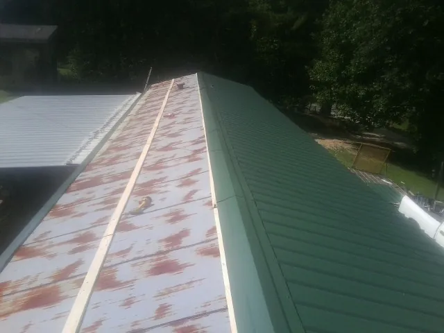 Old rusted panels beside newly installed green metal roofing — Wind Damage Roof Repair by Roofing Brothers in Glen Cove