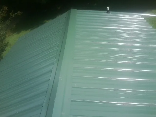 New green metal panels meeting at the ridge of a roof — Flat Roof Repair work by our crew in Glen Cove