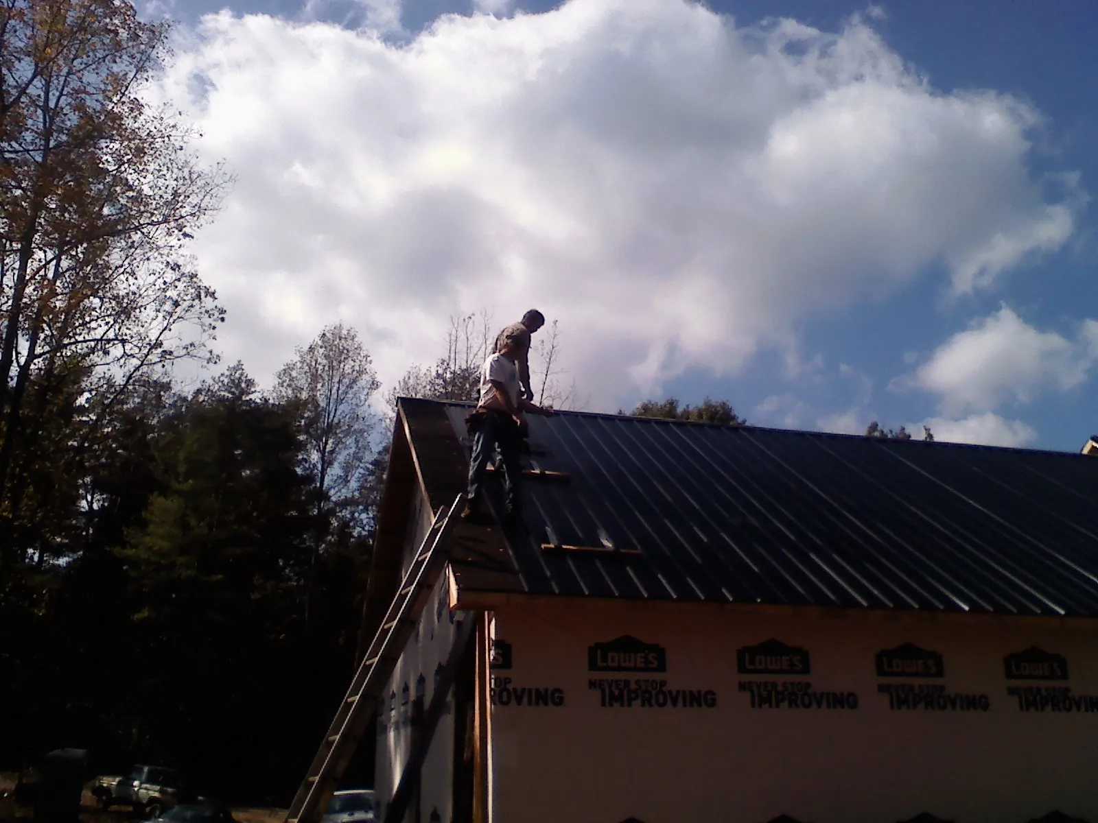 Roofer fastening dark metal panels high against a cloudy sky, from a Roof Inspection job in Glen Cove