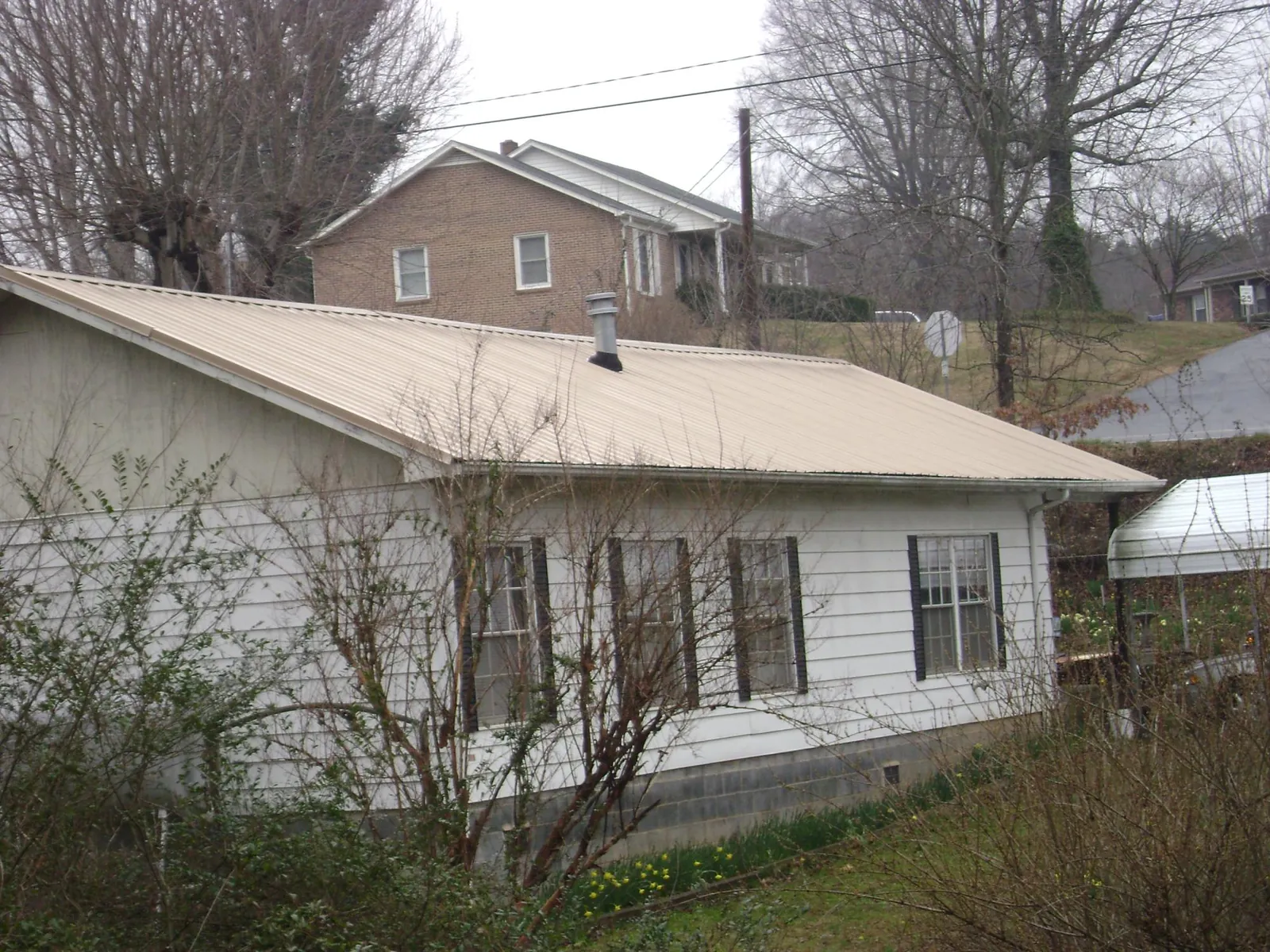 Tan metal roof on a white sided house set into a hillside — Commercial Roofing by Roofing Brothers in Glen Cove
