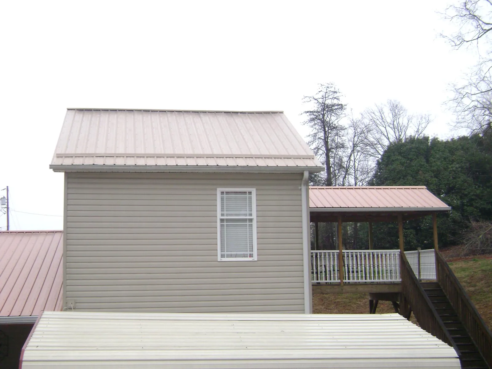 Tan metal roofs on a two story addition and attached porch, from a Roof Replacement job in Glen Cove